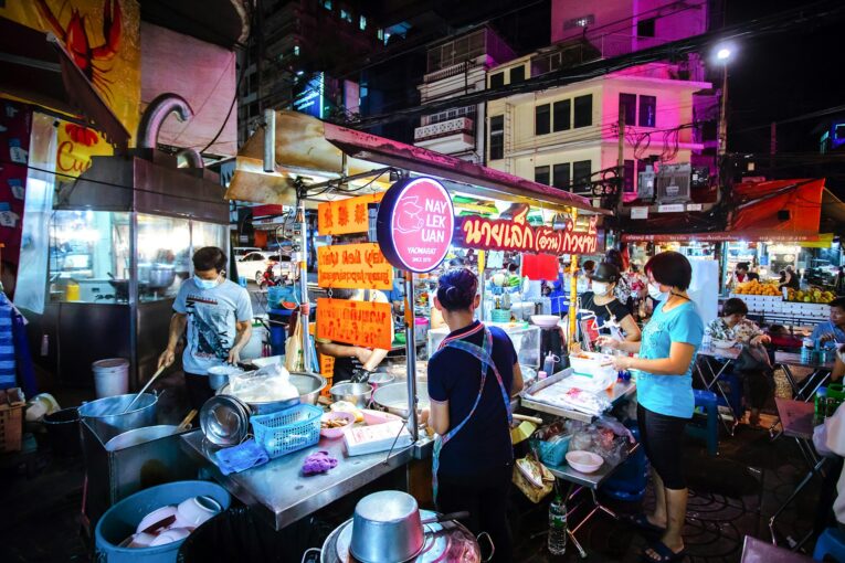 A narrow Bangkok back lane with street food stalls and locals in the evening